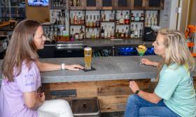 Two women seated at a bar with drinks and chatting