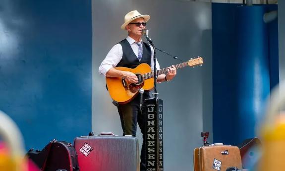 Musician Dean Johanensen on stage, wearing a white hat, and holding his guitar