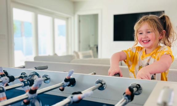 A pony-tailed girl smile as she plays foosball in a local vacation rental