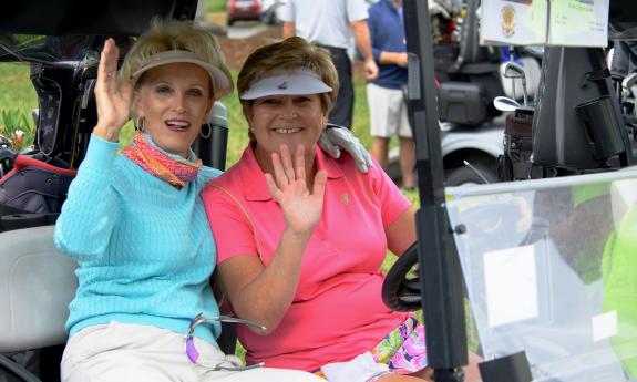 Two women waving from a golf cart