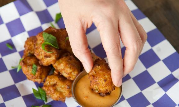 A serving of conch fritters, and a person's hand, dipping the fritter into a white sauce