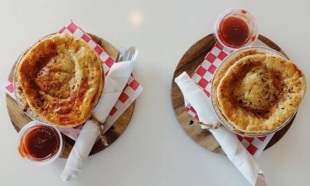 Two Aussie pies with a side of sauces