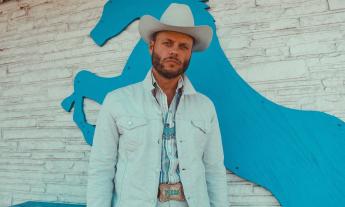 Charley Crockett poses in a blue jean jacket with a matching hat. 