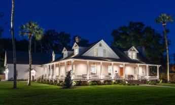 This restored historic plantation house has a wrap-around porch that glows under ceiling lights at night