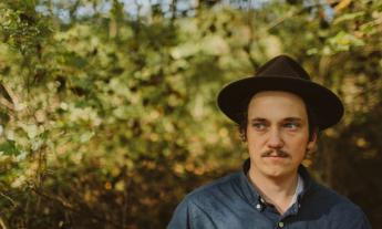 Jonathan Peyton poses in front of a large bush. 