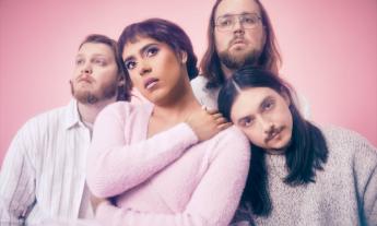 Bandmates from Rainbow Kitten Suprise pose in front of a pink backdrop. 