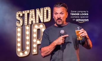 Comedian Zane Lamprey poses on stage with a drink in his hand. 