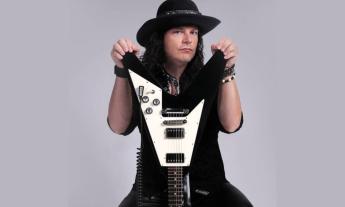 Anthony Gomes wears black clothing while posing with his guitar. 