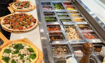 The pizza bar offering a wide selection of veggies, meats, and sauces
