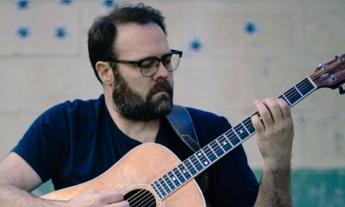 Josh Daniel strums his guitar in front of a gray and teal backdrop. 