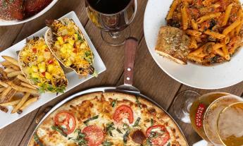 A table spread of pizza, pasta, and tacos