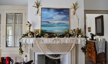 A mantel decorated in an ocean motif with a green boughs, shells. and a fishing net