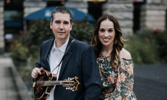 Darin and Brooke Aldridge smile and pose in front of a building with a blue awning. 