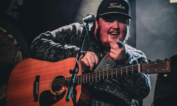 Davis Loose sits on stage with his guitar, smiling as he points toward his fans. 