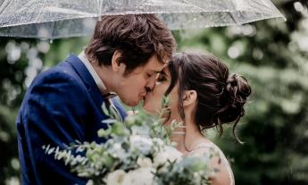 A young bridal couple kiss in the rain, protected by a clear umbrella in the gardens of the Old Powder House Inn Bed and Breakfast