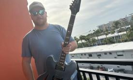 Scott Halls poses with his guitar on a balcony. 