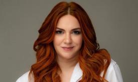 Sarah Ross wears a white blouse while posing in front of a brown backdrop. 