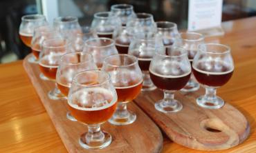 Two wooden trays with small glasses of beer for tasting sitting on a shiny wood bar