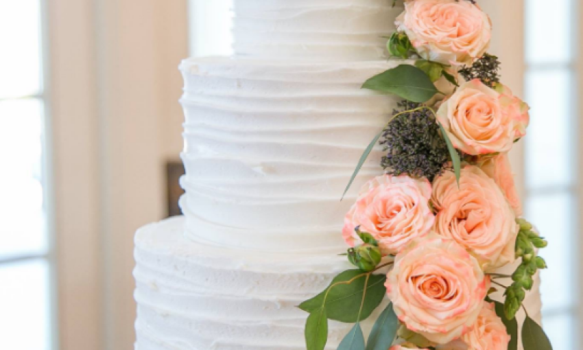 This white, three-tier wedding cake as frosting with a rouched edging, decorated with a cascade of large pink flowers